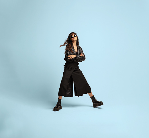 A female model wearing black platform boots, leather jacket, culottes, and sunglasses