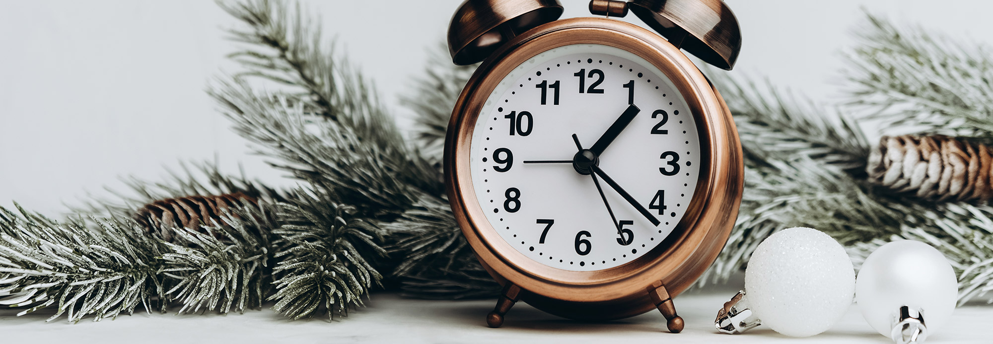 An alarm clock next to snowy pine branches